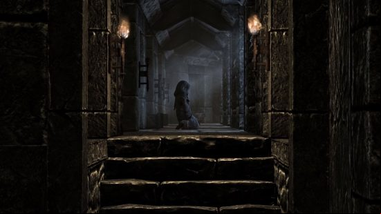 skyrim-console-commands-and-cheats-item-commands Skyrim console commands and cheats: A hooded figure kneels in the middle of a stone hallway, torches and moonlight providing the only source of light.