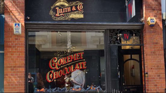 Diablo 4 chocolate shop - Lilith & Co, a storefront promising 'Goremet Chocolate' in gold and red lettering"