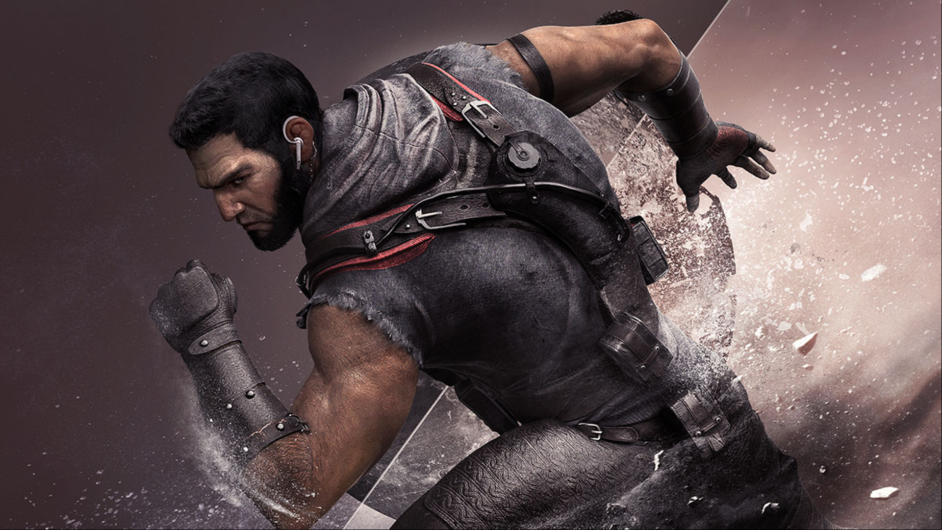 A bearded, short-haired man wearing a grey outfit and arm guards stands flexing