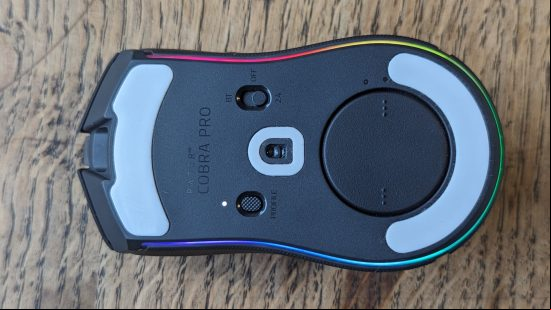 Razer Cobra Pro review: a black mouse with multicolored RGB appears upside-down on a wooden surface.
