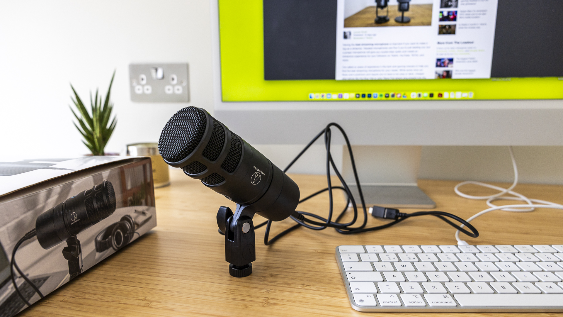 Audio Technica review image showing the microphone on someone's desk near a box and a keyboard.